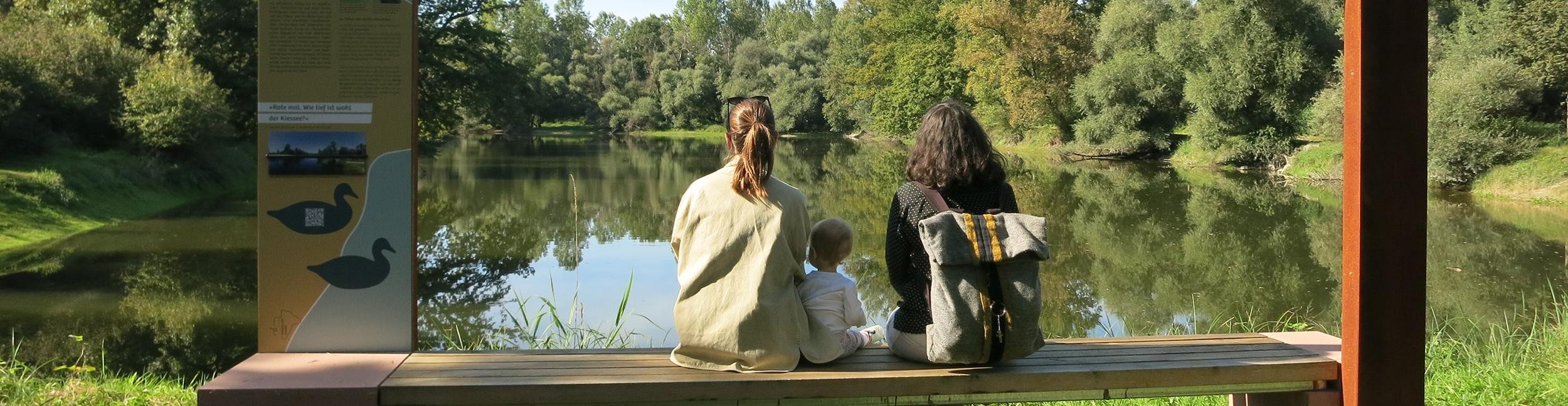 Zwei Frauen und ein Kind sitzen an einer Station der Rheinauen-Runde