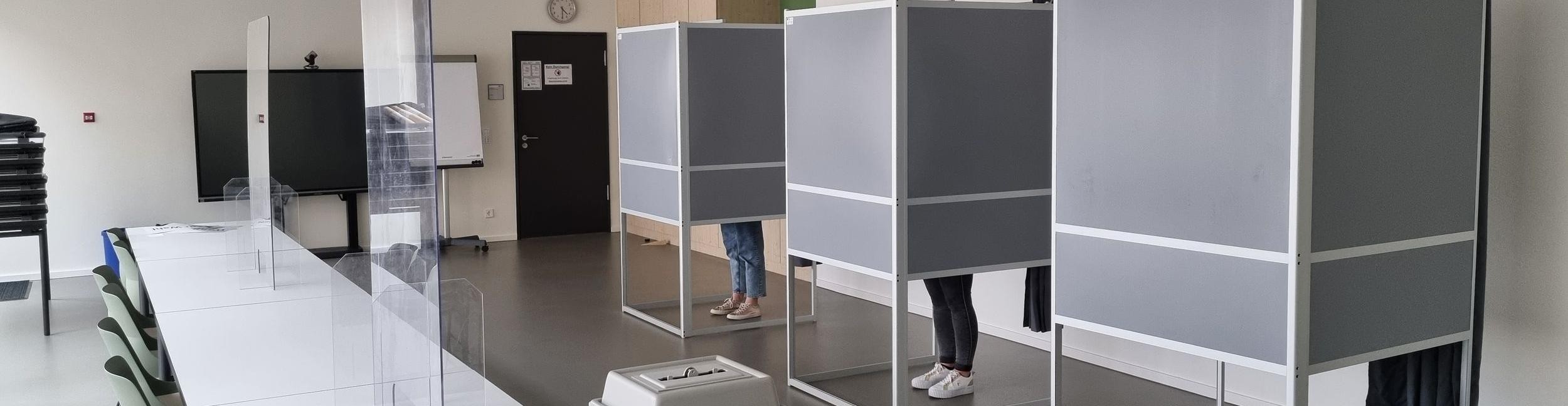 Menschen stehen in der Wahlkabine in einem Wahllokal