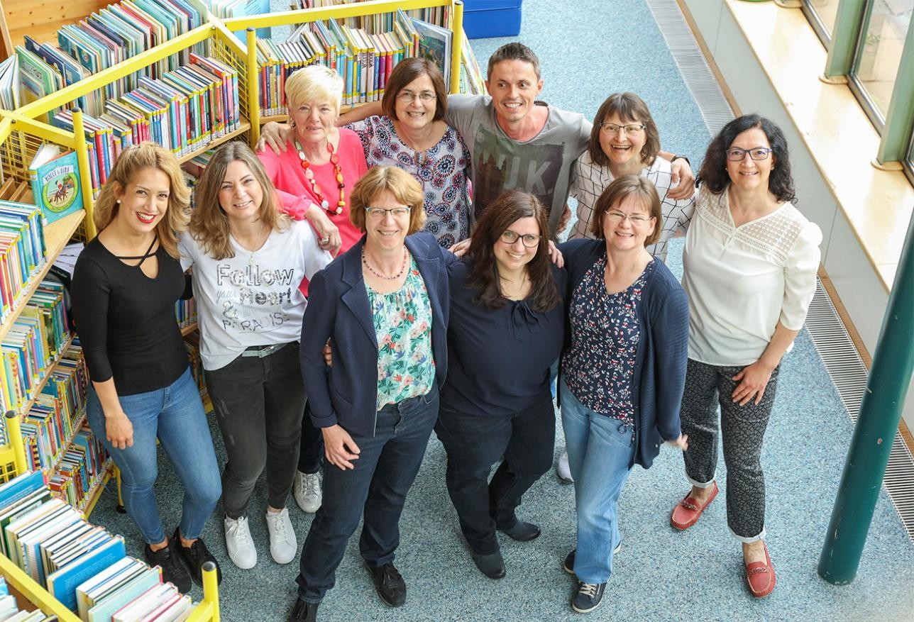 Gruppenfoto der Mitarbeiter der Stadtbibliothek, 10 Frauen und 1 Mann, im im Hintergrund Regale mit Büchern. 