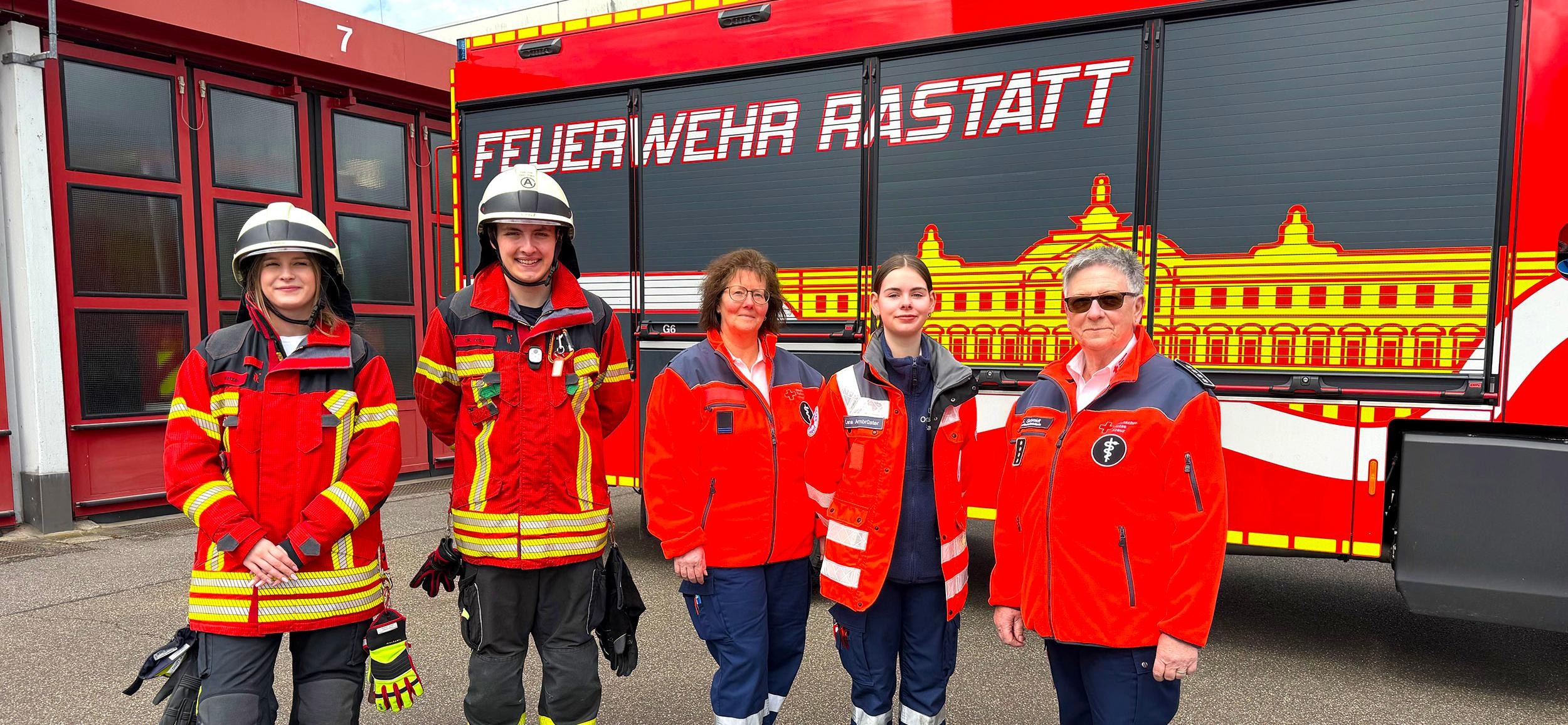 Feuerwehrleute und Frauen vom DRK stehen vor einem Feuerwehrauto