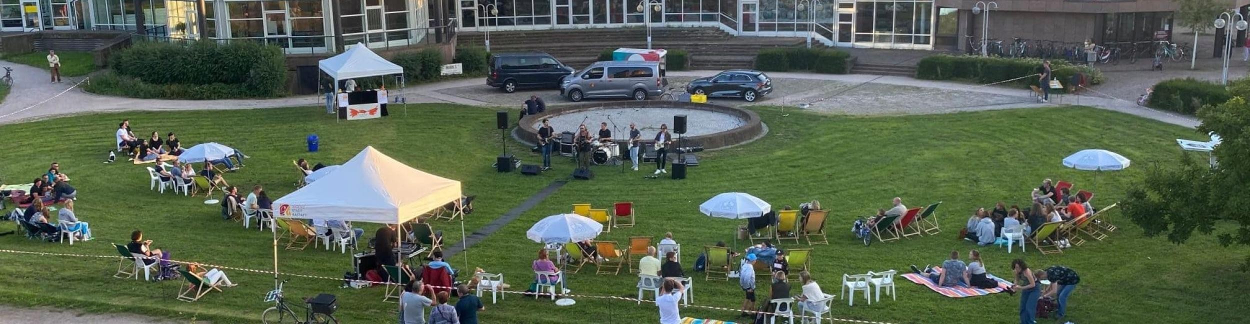 Murgchillout Rastatt - On a meadow many people sit on deck chairs, in front of it a band plays music, in the background buildings