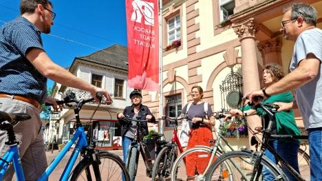 Groupe de cyclistes devant la mairie d'Hisror, sur la place du marché, discutant de l'itinéraire à suivre