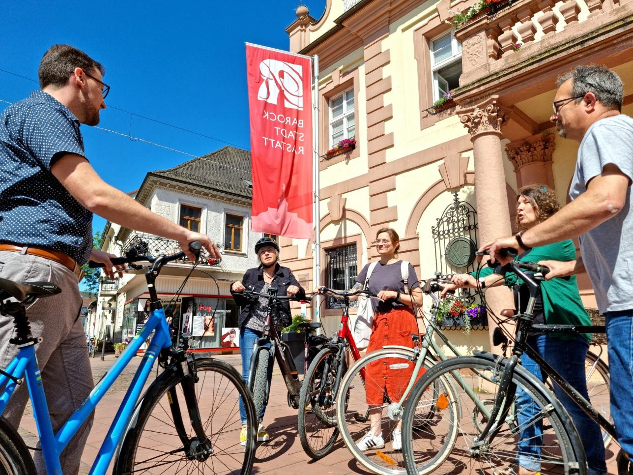 Group of cyclists stand in front of the historic town hall and discuss the route
