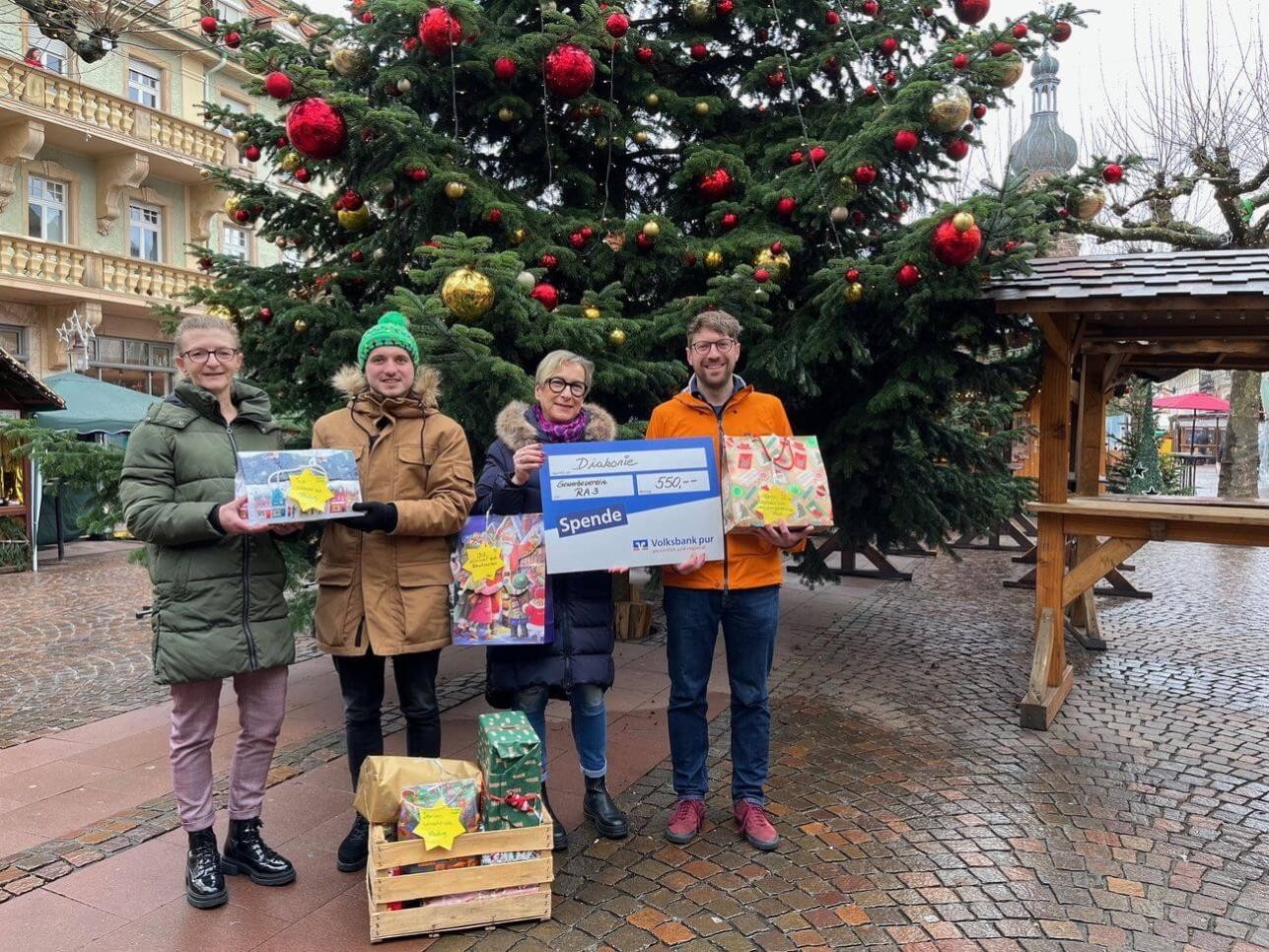 Menschen mit Geschenken in der Hand vor dem Wunschbaum auf dem Marktplatz