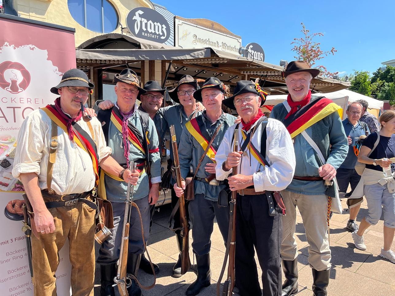 Actors stand in front of a beer cart in front of the riding hall