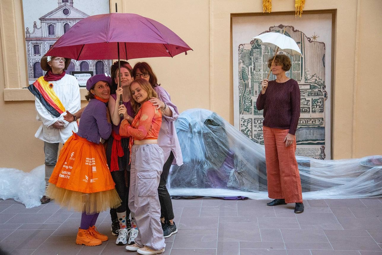Dancers stand under an umbrella