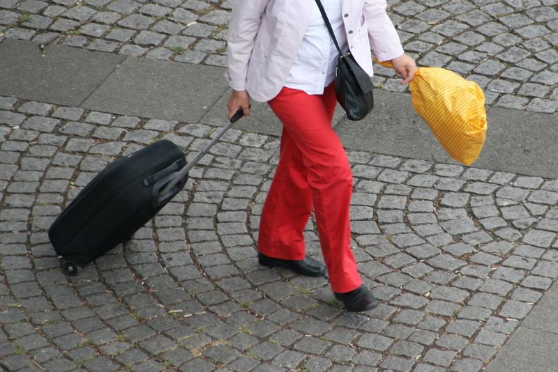 Eine Frau trägt einen gelben Blumenstrauß, eine rote Hose und einen schwarzen Koffer