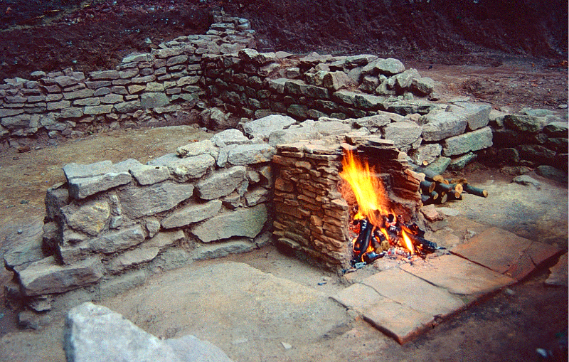 Mauerreste mit einem kleineren ummauerten Raum in welchem ein Feuer brennt